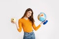 A beautiful young girl in a yellow sweater is holding a globe and a camera. Recreation, travel, tourism Royalty Free Stock Photo