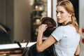 Beautiful young hairstylist looking at camera while combing and cutting hair to male client Royalty Free Stock Photo