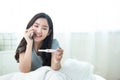 Beautiful young happy  asian woman holding pregnant positive test in hand and using smart mobile phone with smile while sitting on Royalty Free Stock Photo