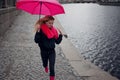 Beautiful young and happy blond woman in a bright pink scarf, rubber boots and umbrella walking in a rainy city. Royalty Free Stock Photo