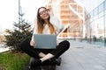 Beautiful young happy business woman posing sitting outdoors near business center wearing eyeglasses using laptop computer Royalty Free Stock Photo