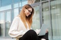 Beautiful young happy business woman posing sitting outdoors near business center wearing eyeglasses using laptop computer Royalty Free Stock Photo