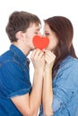 Beautiful young happy couple kissing behind a red heart, holding it in hands, isolated on a white background Royalty Free Stock Photo