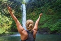 Beautiful young happy girl enjoying nature under tropical fresh waterfall