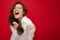 Beautiful young happy joyful funny curly brunette woman wearing white shirt and optical glasses isolated on red Royalty Free Stock Photo