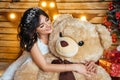 Beautiful young happy woman in a festive mood waiting for new year and Christmas, sitting with a big toy bear Royalty Free Stock Photo