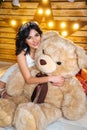 Beautiful young happy woman in a festive mood waiting for new year and Christmas, sitting with a big toy bear Royalty Free Stock Photo