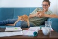 Beautiful young happy woman in glasses uses a smartphone on the couch, a cute red cat lap Royalty Free Stock Photo