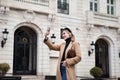 Beautiful young happy woman tourist takes selfie against beautiful architecture building while traveling on historic