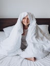 Beautiful young happy woman wrapped in soft white blanket sitting at home. Winter atmosphere. Millennial Caucasian girl Royalty Free Stock Photo