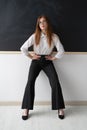 Beautiful young high school teacher in the office. She is standing in front of a clean black board. She is wearing a Royalty Free Stock Photo