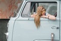 A beautiful young hippie woman in yellow sunglasses looks out the window of a blue vintage minivan. Make love, not war Royalty Free Stock Photo