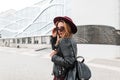 Beautiful young hipster woman in dark sunglasses in a vintage purple hat in a leather jacket with a black stylish backpack walks Royalty Free Stock Photo
