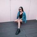 Beautiful young hipster woman in a fashionable denim jacket in a blue skirt in a T-shirt in trendy leather black boots Royalty Free Stock Photo