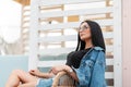 Beautiful young hipster woman in fashionable sunglasses in a black t-shirt in a stylish denim jacket in a skirt relaxes sitting Royalty Free Stock Photo