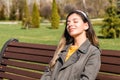 Beautiful young hipster woman sitting on bench in park with eyes closed enjoying spring sun beams Royalty Free Stock Photo