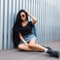 Beautiful young hipster woman in a trendy denim jacket in a blue skirt in a T-shirt in stylish leather black boots in sunglasses Royalty Free Stock Photo