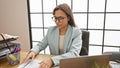 Beautiful young hispanic woman immersed in success, bossing the business world at her office desk, serious yet relaxed, reading