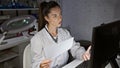 Beautiful young hispanic woman, a serious scientist in the lab, immersed in science research on her computer, reading document Royalty Free Stock Photo