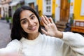 A beautiful young Indian woman in a white sweater is standing on a city street and talking on a video call on a Royalty Free Stock Photo