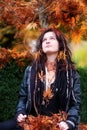 Beautiful young individual, eccentric woman, with dreadlocks, piercing and tattoo, wearing a black leather jacket, sits