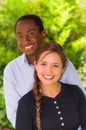 Beautiful young interracial couple in garden environment, embracing and smiling happily to camera Royalty Free Stock Photo