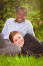 Beautiful young interracial couple in sitting garden environment, embracing and smiling happily to camera Royalty Free Stock Photo