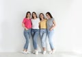 Beautiful young ladies in jeans and colorful t-shirts near white wall. Woman`s Day Royalty Free Stock Photo