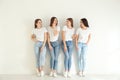 Beautiful young ladies in jeans and white t-shirts near wall indoors. Woman`s Day Royalty Free Stock Photo