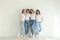 Beautiful young ladies in jeans and white t-shirts near light wall. Woman`s Day Royalty Free Stock Photo