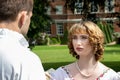 Beautiful young lady dressed in period costume confronting her husband or lover with stately home in background.