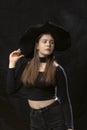 Beautiful young lady wears black clothes and wide-brimmed hat. Portrait of young model on black background. Vertical frame Royalty Free Stock Photo