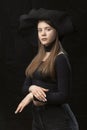 Beautiful young lady wears black clothes and wide-brimmed hat. Portrait of young modern aristocrat on black background. Vertical Royalty Free Stock Photo