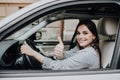 Beautiful young woman driving her brand new car and showing her thumb up Royalty Free Stock Photo