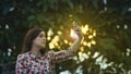 Beautiful young latin woman in floral design dress taking a selfie in the garden at sunset with the sun`s rays passing through th