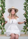 Beautiful young leggy blonde in a little white dress and white cowboy hat on a swing, wooden swing suspended from a rope Royalty Free Stock Photo