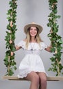 Beautiful young leggy blonde in a little white dress and white cowboy hat on a swing, wooden swing suspended from a rope Royalty Free Stock Photo