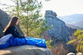 Woman sitting alone in sleeping bag on big mountain rock and smiling