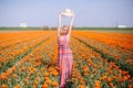 Beautiful young long red hair woman wearing in striped dress and straw hat standing on colorful flower tulip field in Holland Royalty Free Stock Photo