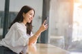 Beautiful young millennial Asian woman using a smartphone at a cafe. Portrait of a gorgeous smiling female engrossed in Royalty Free Stock Photo