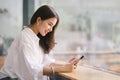 Beautiful young millennial Asian woman using a smartphone at a cafe. Portrait of a gorgeous smiling female engrossed in Royalty Free Stock Photo