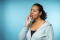 Beautiful young mixed race woman in casual clothing eating and enjoying a fresh strawberry with a blue background Royalty Free Stock Photo