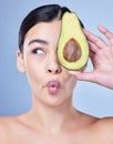 A beautiful young mixed race woman holding a sliced avocado. Hispanic model with glowing skin holding a fruit against a