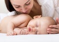 Beautiful young mom looking at her sleeping little baby and smiling. Child lying in bed at home Royalty Free Stock Photo