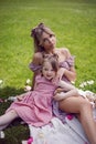 beautiful young mother with a baby daughter in pink dresses sitting on a plaid in a green meadow in nature with a picnic Royalty Free Stock Photo