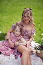beautiful young mother with a baby daughter in pink dresses sitting on a plaid in a green meadow in nature with a picnic Royalty Free Stock Photo