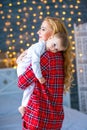 A beautiful young mother in checkered pajamas holds a little son in her arms. Caring and motherly love Royalty Free Stock Photo