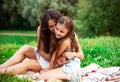 Beautiful young mother embracing and kissing her cute long hair daughter on summer green grass background