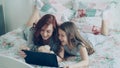 Beautiful young mother and her cute daughter in pajamas laughing and looking in digital tablet while lying on bed at Royalty Free Stock Photo