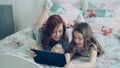 Beautiful young mother and her cute daughter in pajamas laughing and looking in digital tablet while lying on bed at Royalty Free Stock Photo